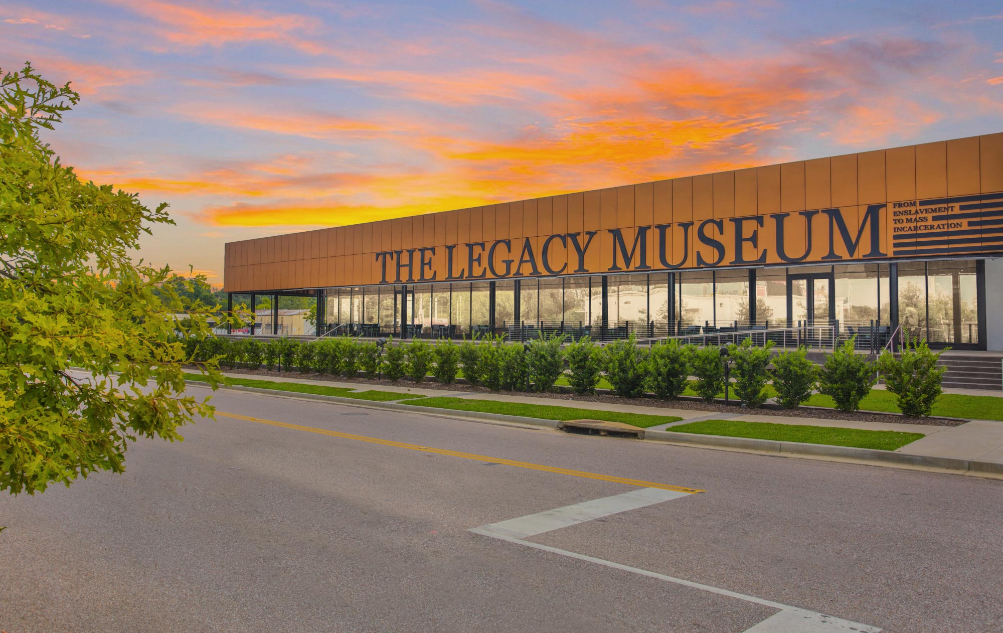The front of the Legacy Museum with a striking gold, pink, and orange sunset behind.