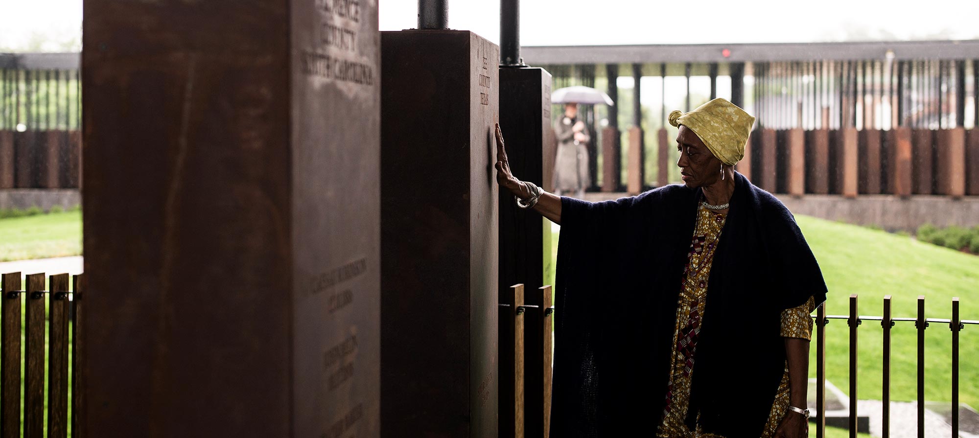 A woman solemnly places her hand on a monument in the National Memorial for Peace and Justice that recognizes the racial terror lynching of her ancestor.