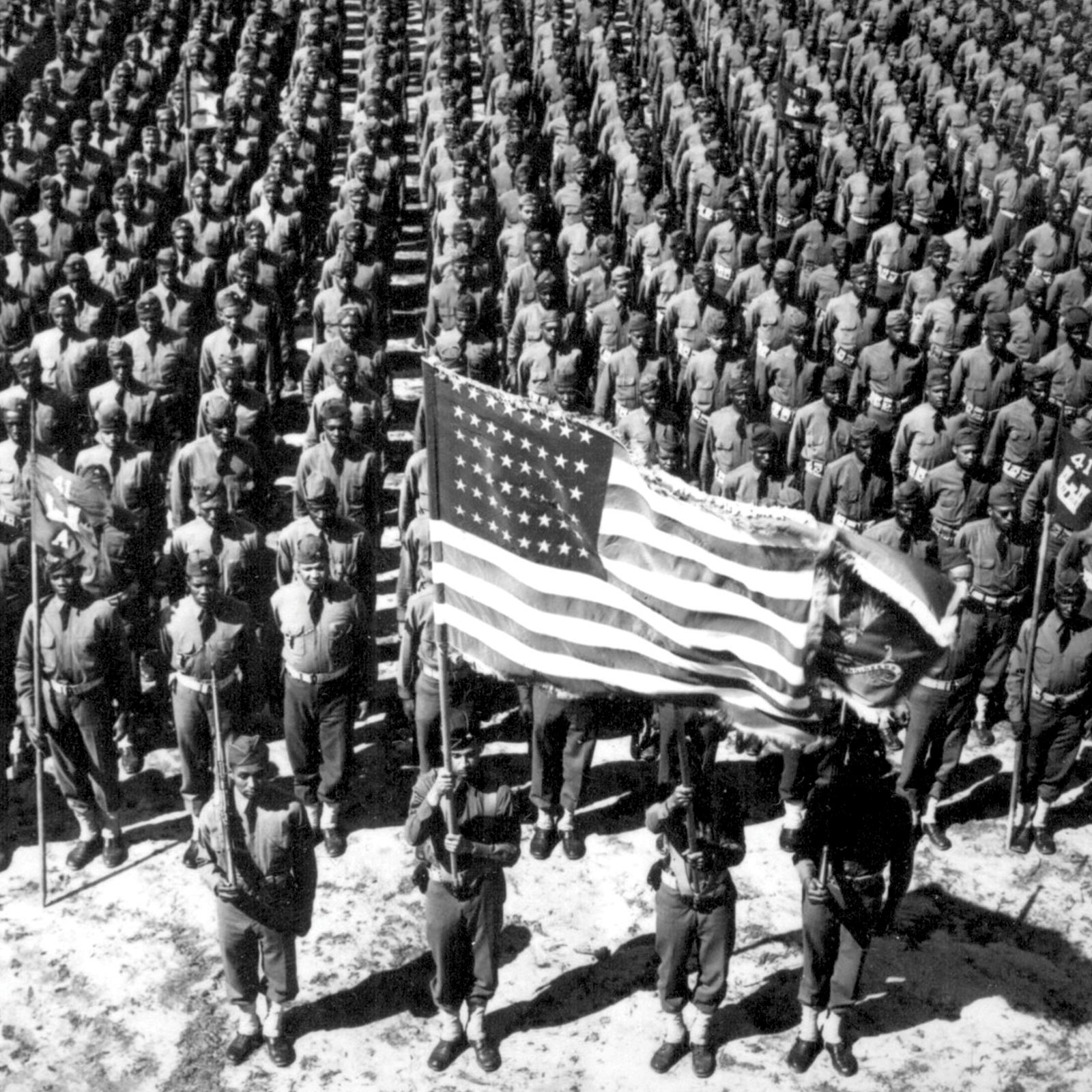 Black troops line up in formation in front of a color guard with a large American flag.