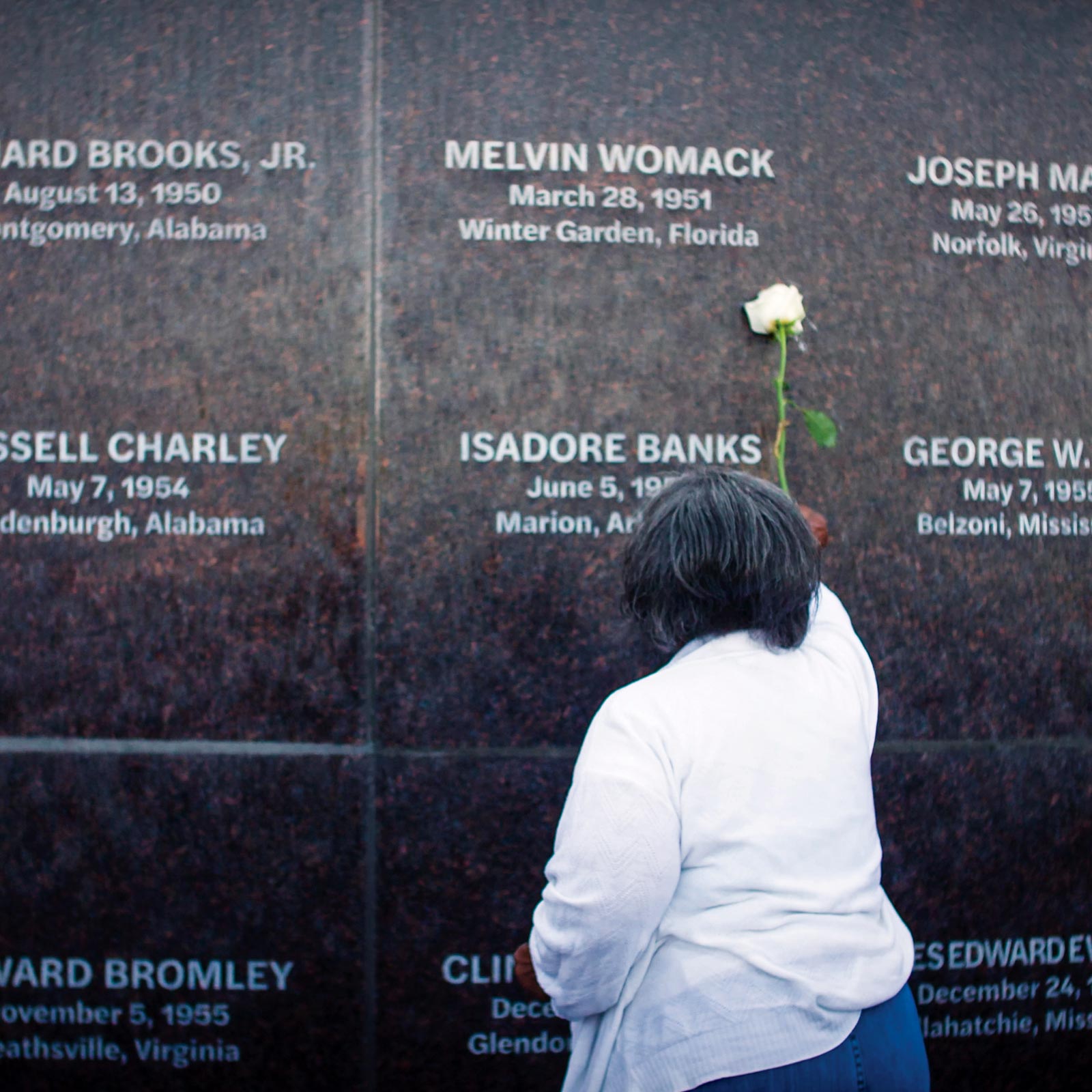A woman touches a white rose to the monument at the Peace and Justice Memorial Center to honor a family member who was lynched during the 1950s.