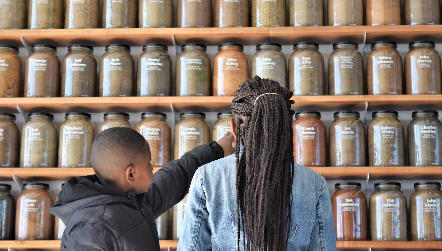 A young boy points out to his older sister one jar from a wall of jars containing soil from the sites of racial terror lynchings in Alabama.