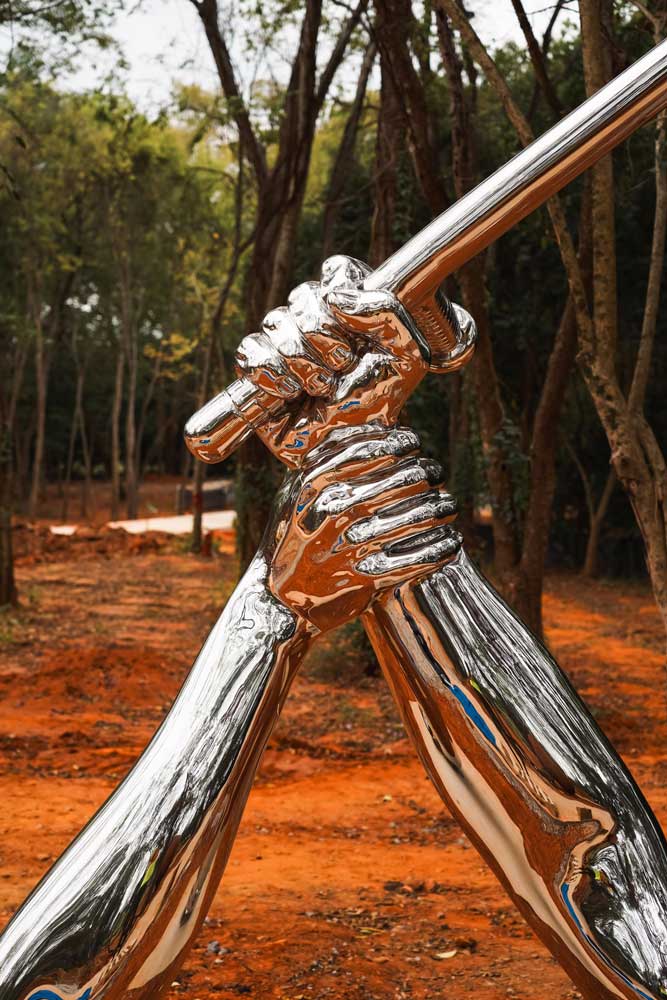 Shiny, reflective silver sculpture by Hank Willis Thomas called Strike, which shows one hand and arm defensively grasping a second arm that is swinging a police baton or nightstick, to stop the blow.