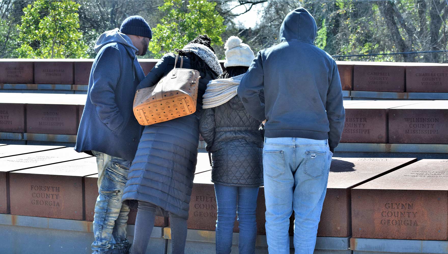A family examines the names and dates of lynching victims inscribed on a corten steel monument in Monument Park at the National Memorial for Peace and Justice.